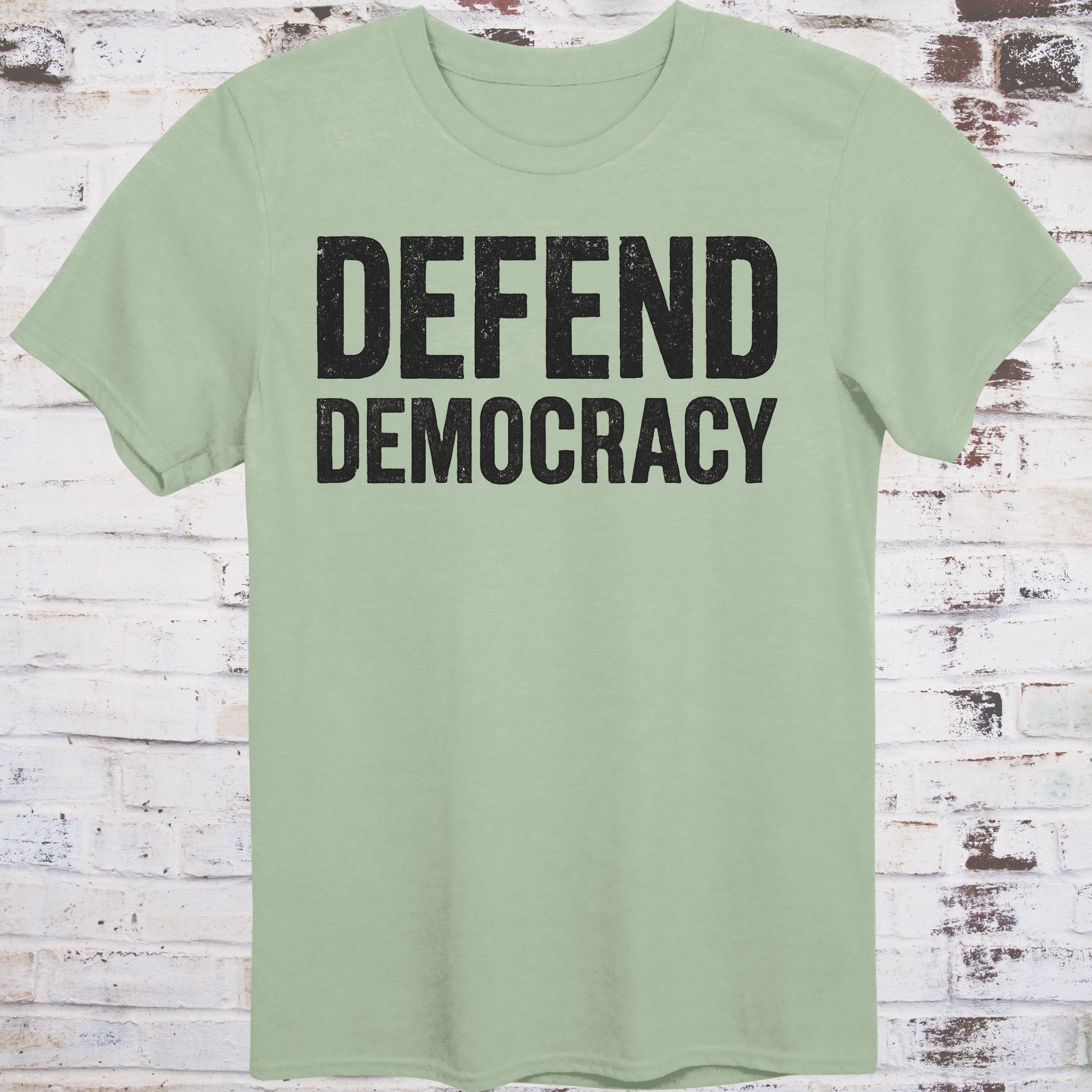 Light green t-shirt with 'DEFEND DEMOCRACY' text on a wooden background