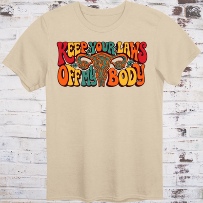 Keep Your Laws Off My Body in massive interlocking 70s bubble letters in deep red, teal, and orange around a stylized uterus, on a warm mustard yellow background.